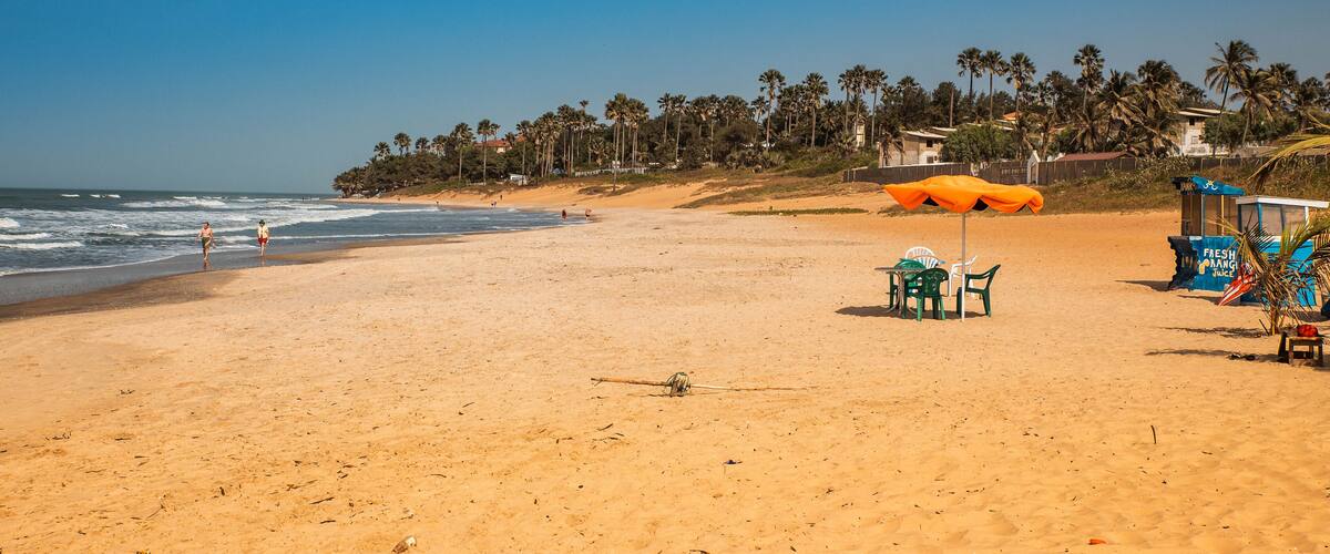 A sandy beach with palm trees, a lifeguard tower, and a few people walking.