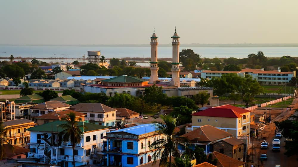 A coastal town with a prominent mosque featuring two minarets, surrounded by residential buildings and palm trees.