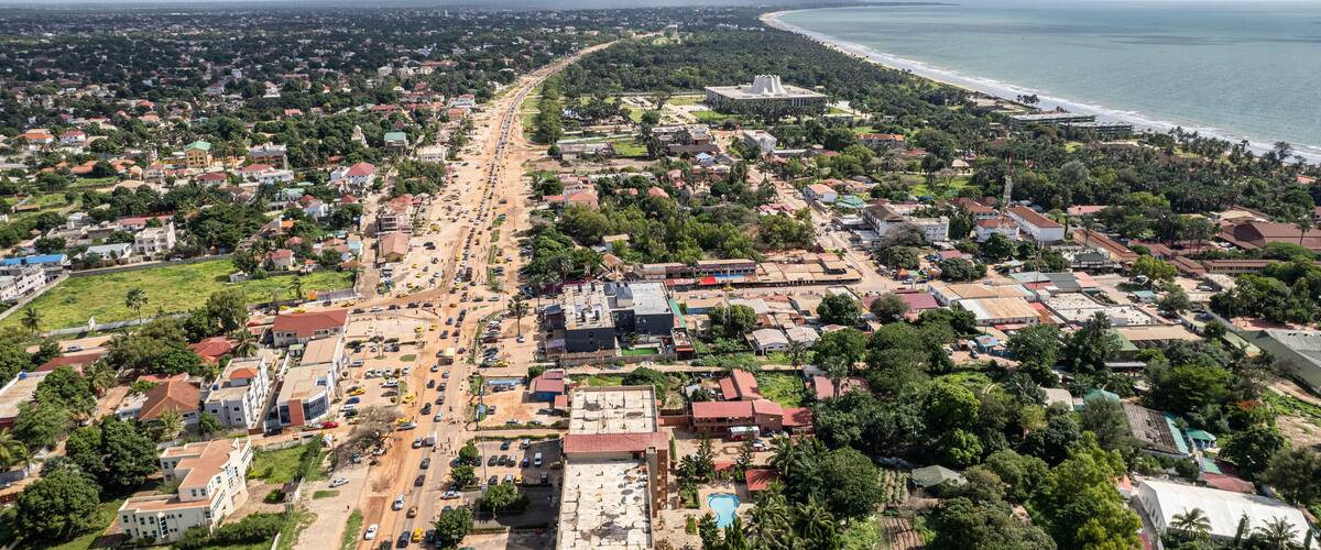 Aerial view of bustling urban landscape with houses, cars, and trees near the coastline, Kololi, The Gambia.