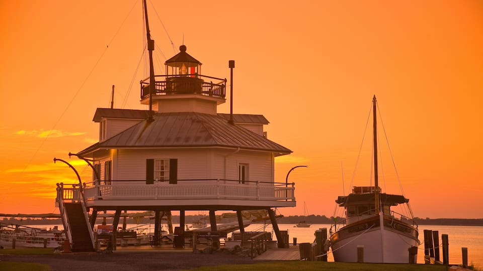 A lighthouse at sunset with a boat docked nearby.