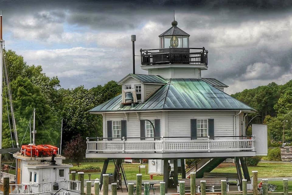 A lighthouse on stilts with a green roof, surrounded by water and greenery.
