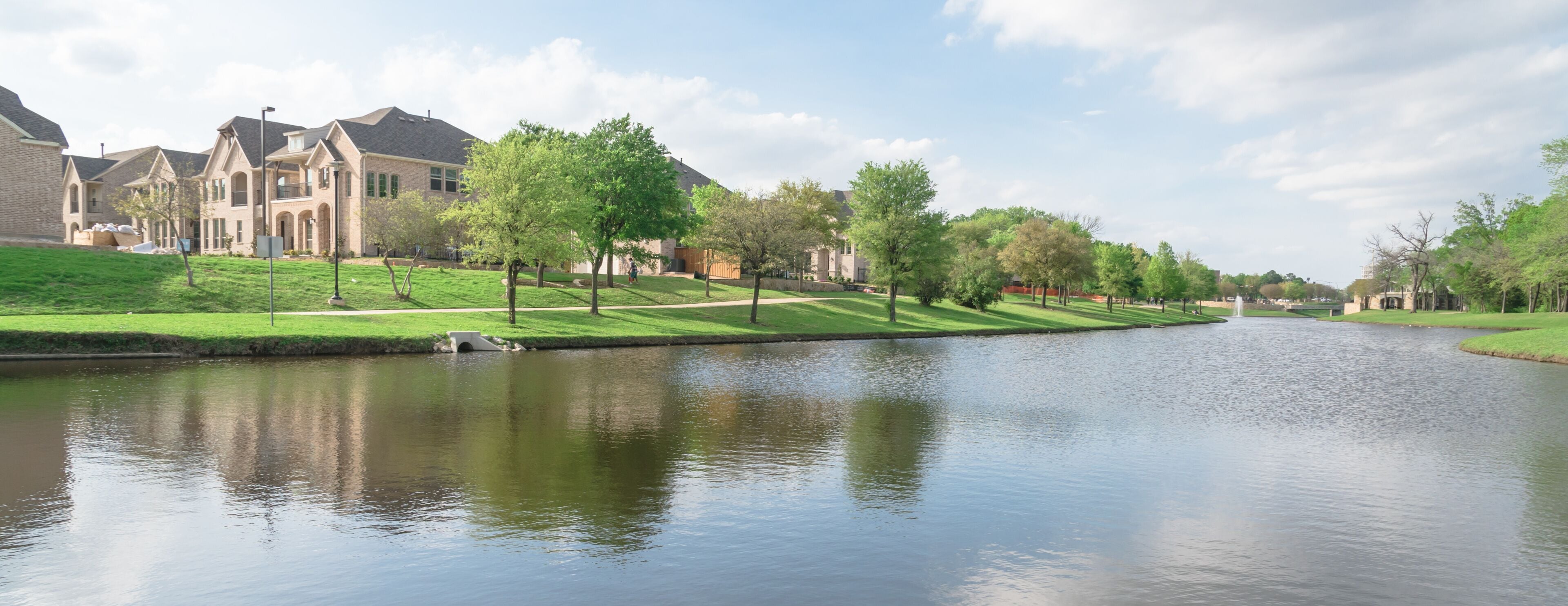 Typical lakeside new-established community with newly built detached single-family homes. Cloud blue sky reflection near urban park in suburban Irving, Texas, USA. Panorama view