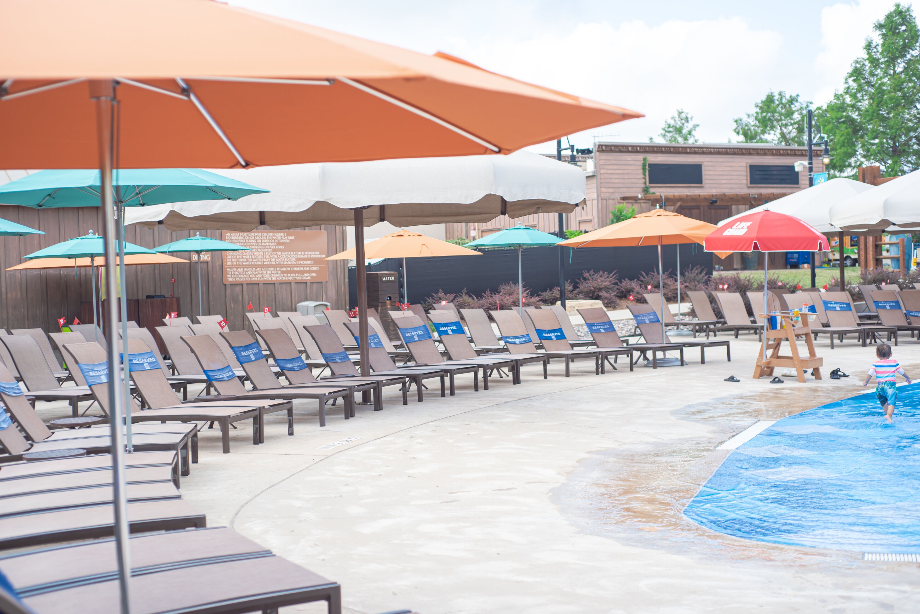Upscale hotel swimming pool with row of pool lounge chairs reserved words wrap around, small plastic service flag with number in Grapevine, Texas, colorful beach umbrella, summer holiday event