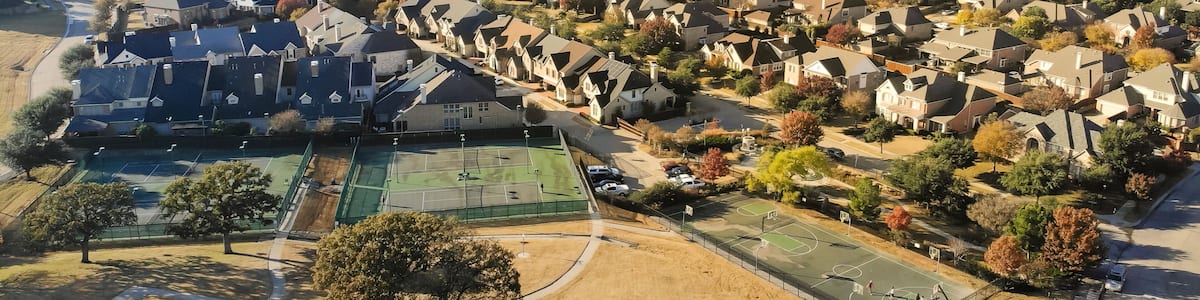 A residential area with houses, a tennis court, and autumn-colored trees.