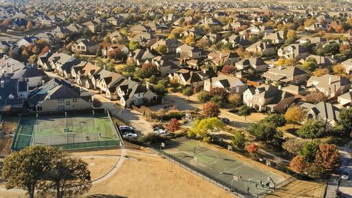 Un barrio residencial con casas, una cancha de tenis y árboles de colores otoñales.