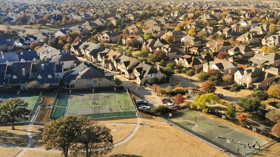 A residential area with houses, a tennis court, and autumn-colored trees.