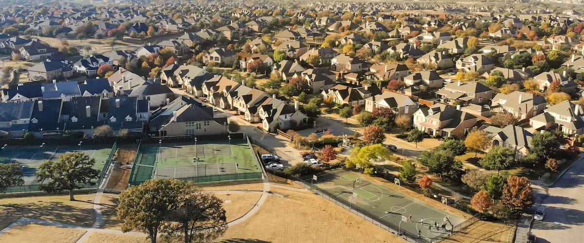 A residential area with houses, a tennis court, and autumn-colored trees.