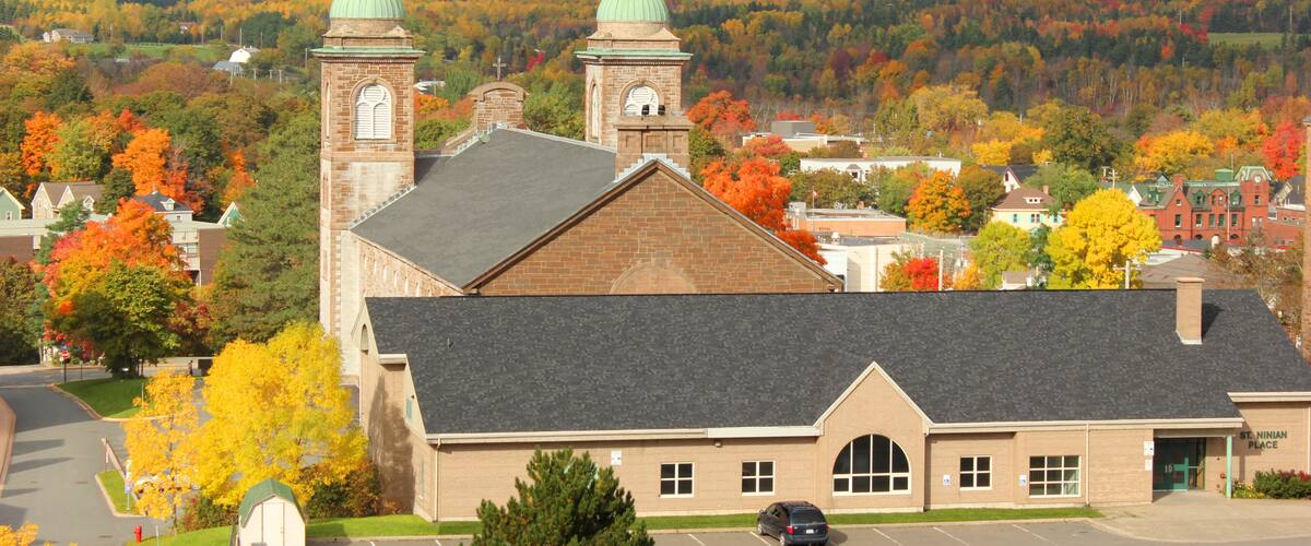 A church with two towers and a green dome, surrounded by autumn-colored trees and a hilly landscape.