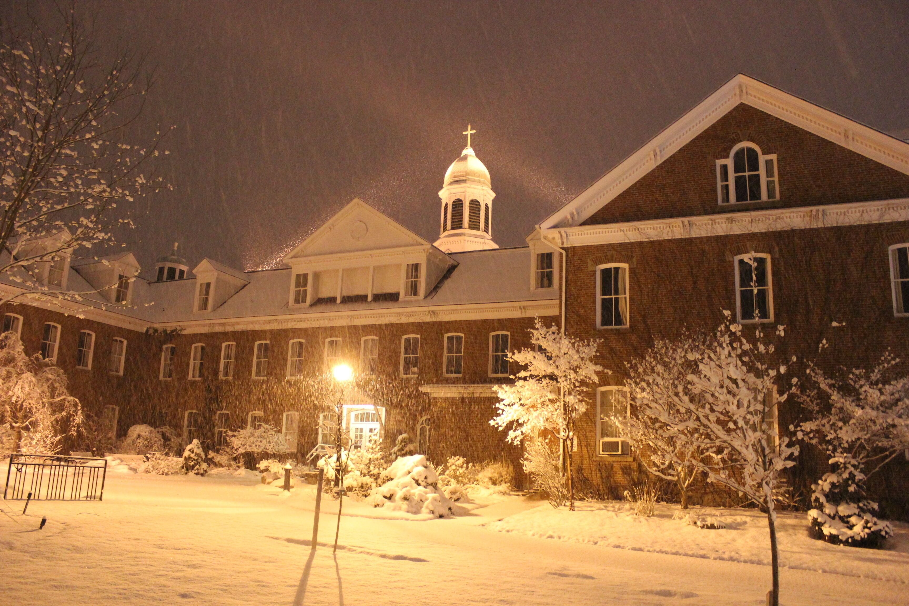 A snow-covered building with a dome and a cross on top, surrounded by snow-laden trees and a fence.