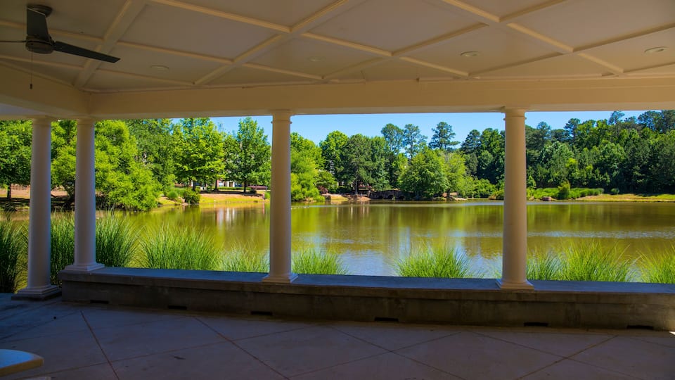 A covered pavilion with columns overlooking a calm lake surrounded by trees.