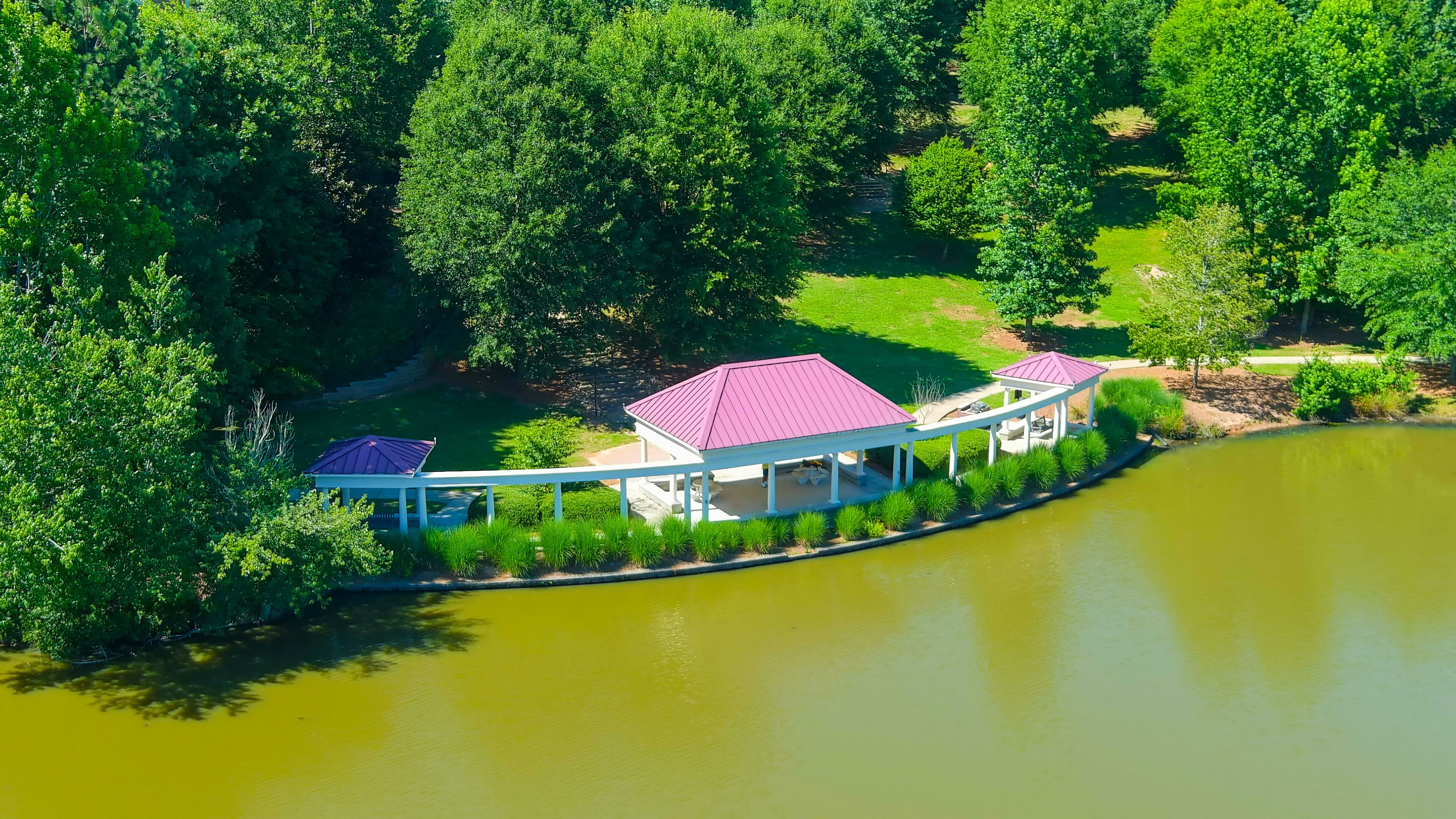 A lakeside pavilion with a red roof, surrounded by lush greenery and trees.