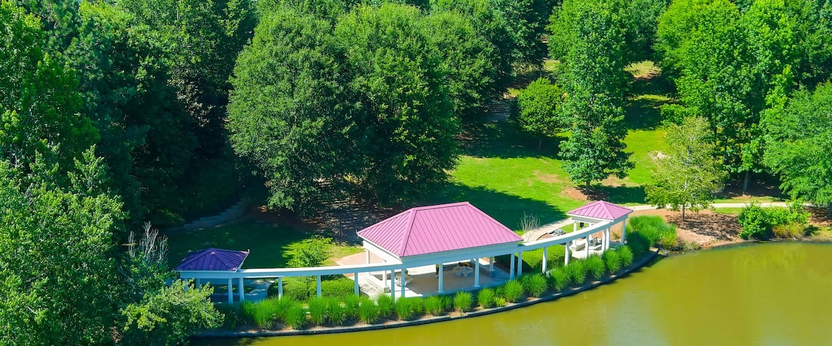 A lakeside pavilion with a red roof, surrounded by lush greenery and trees.