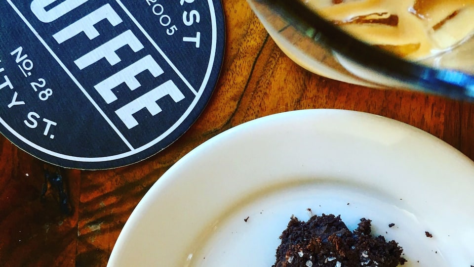 A coaster with "AMHERST COFFEE" and "No. 28" on it, a glass with a creamy beverage, and a plate with a piece of cake.