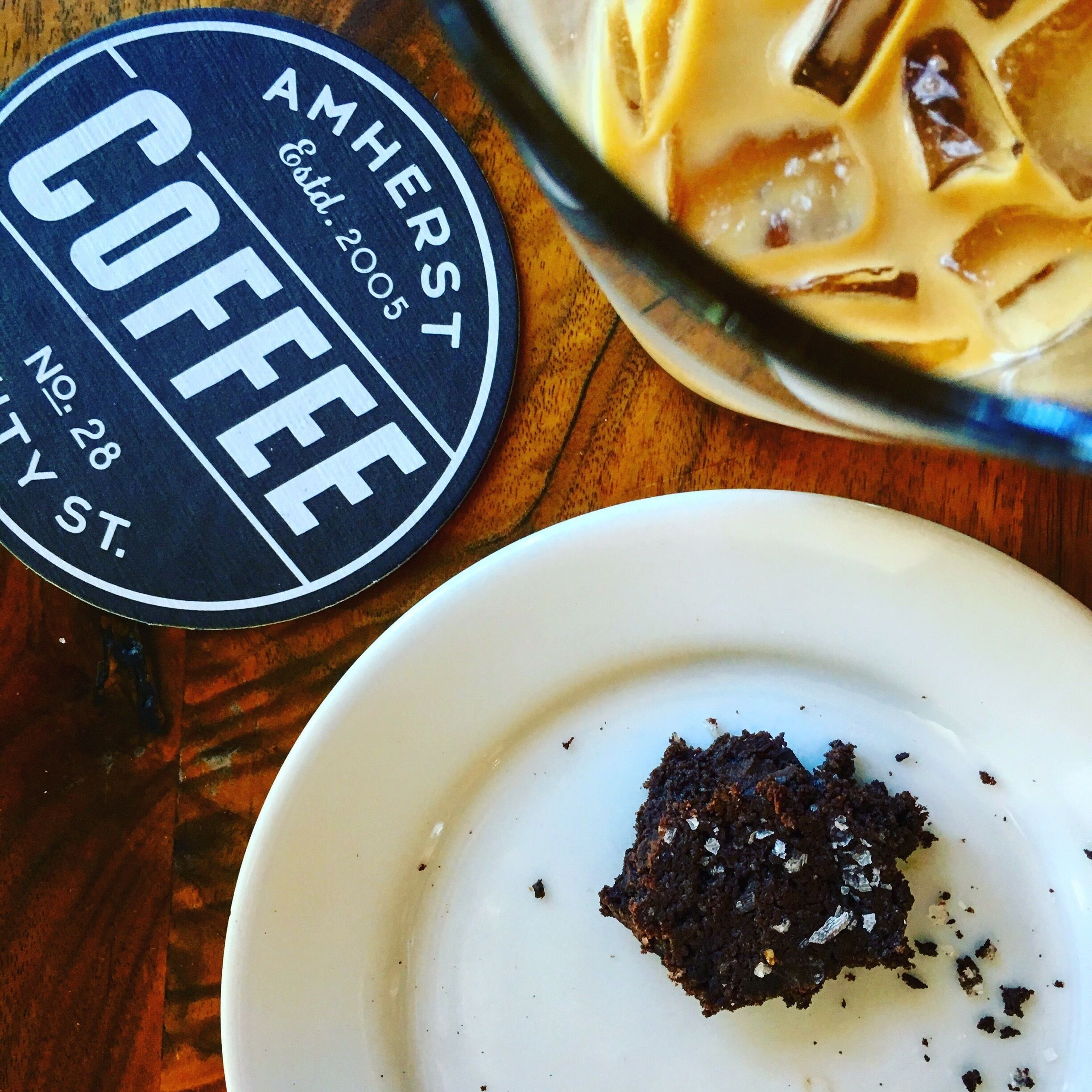 A coaster with "AMHERST COFFEE" and "No. 28" on it, a glass with a creamy beverage, and a plate with a piece of cake.