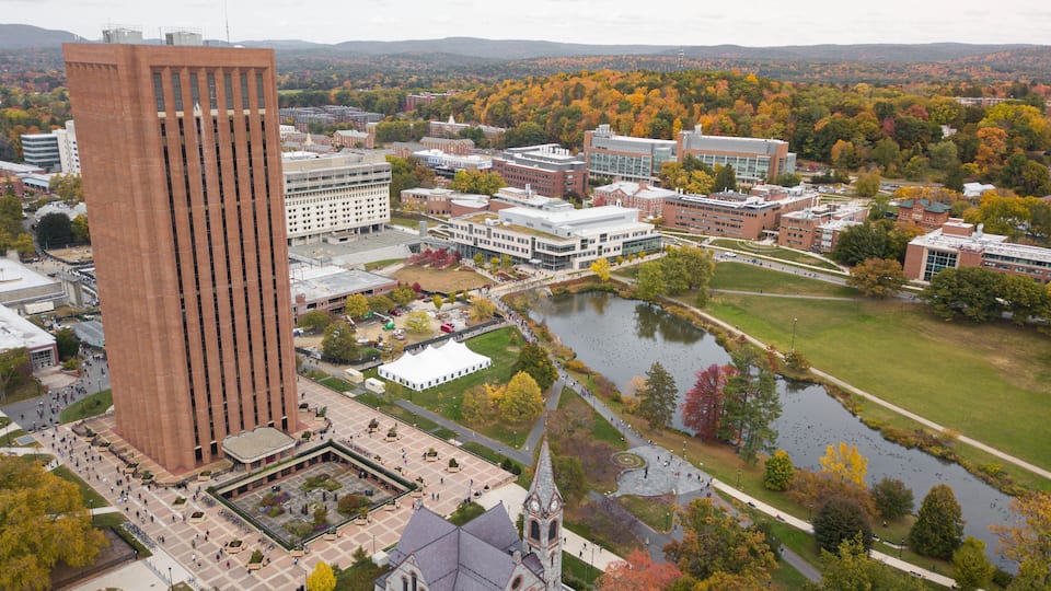 A university campus with a prominent red building, a historic church, and a river.