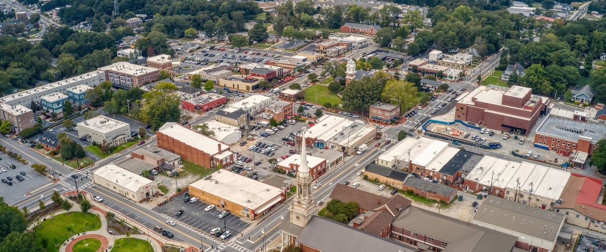 An aerial view of a town with a central square, surrounding buildings, and a large parking lot.