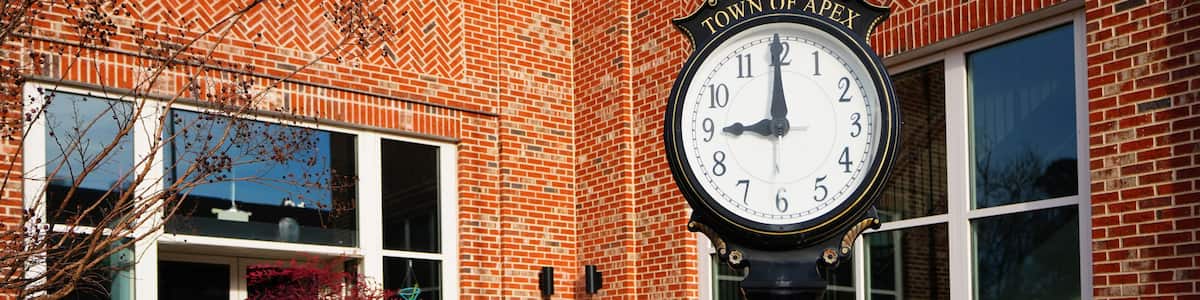 A clock with 'TOWN OF APEX' on a brick building.