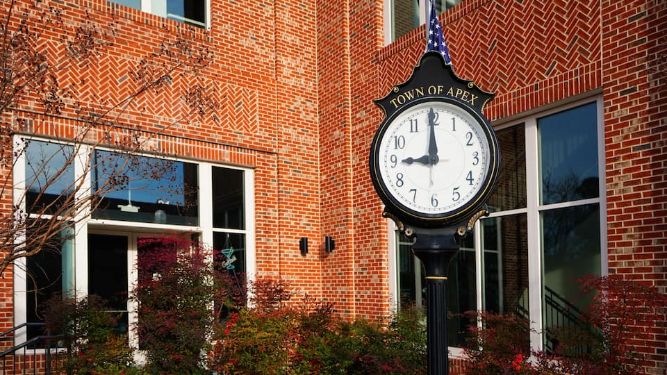 A clock with 'TOWN OF APEX' on a brick building.