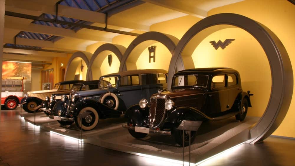 A museum display of vintage cars in a well-lit, arched gallery with a yellow wall and a large 'W' logo.