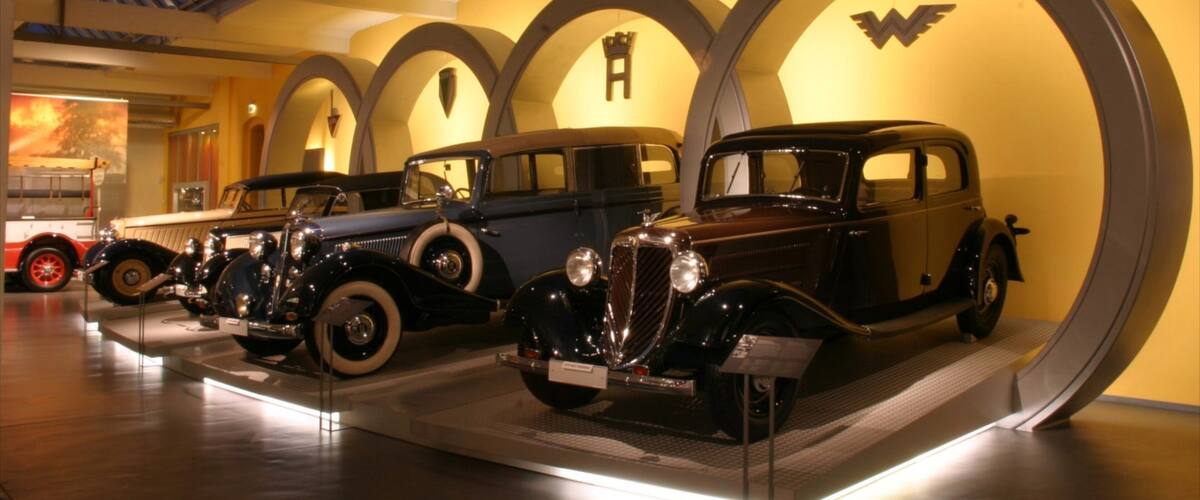 A museum display of vintage cars in a well-lit, arched gallery with a yellow wall and a large 'W' logo.