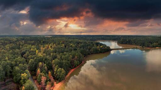 a stunning panoramic shot of the silky brown waters of the Chattahoochee river surrounded by green and autumn colored trees with powerful clouds at Sweetwater Creek State Park in Lithia Springs GA