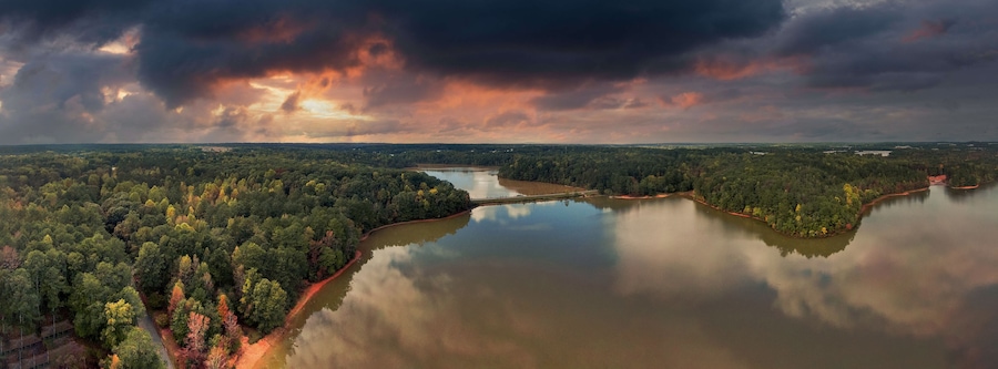 a stunning panoramic shot of the silky brown waters of the Chattahoochee river surrounded by green and autumn colored trees with powerful clouds at Sweetwater Creek State Park in Lithia Springs GA
