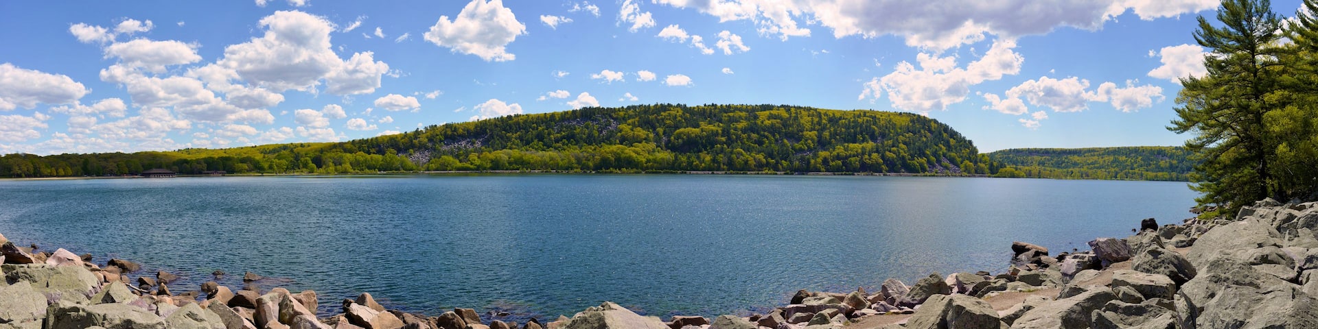 A calm lake surrounded by rocky shores and a forested hill.