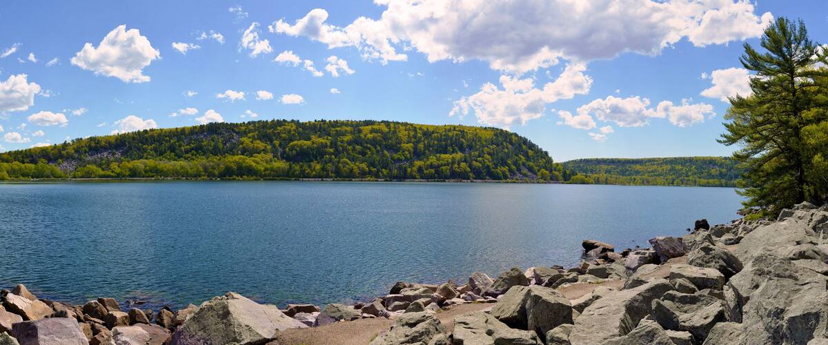 A calm lake surrounded by rocky shores and a forested hill.