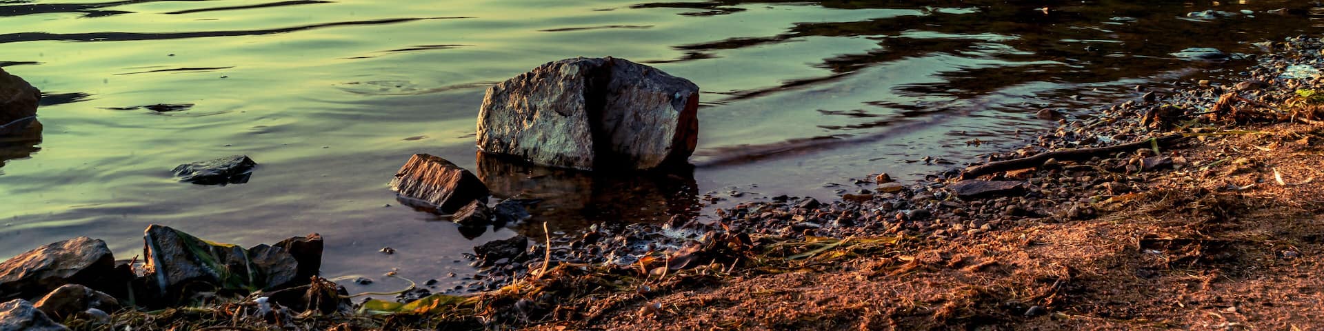 A small boulder protruding from the surface of the water as the sun sets over Devil's Lake in Baraboo, Wisconsin USA.