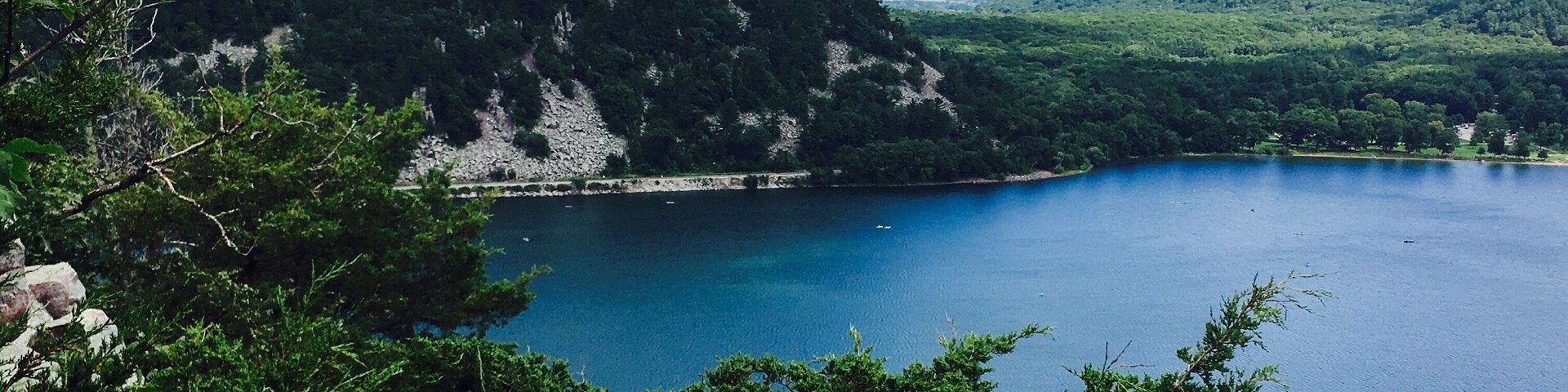 A lake surrounded by lush green hills and a rocky cliff.
