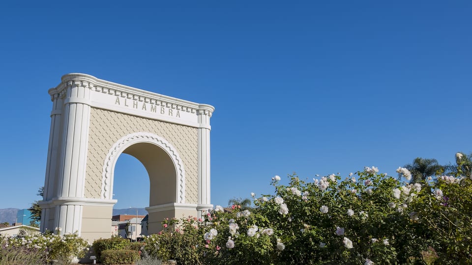 An archway with the inscription "ALHAMBRA" against a clear blue sky.