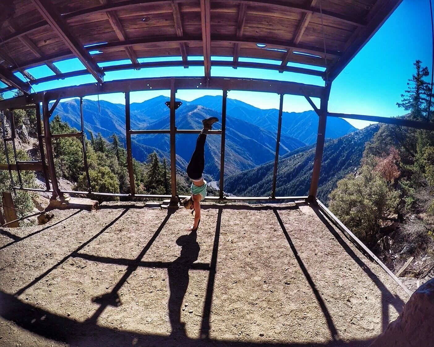A person performing a handstand against a backdrop of mountains and a clear sky.
