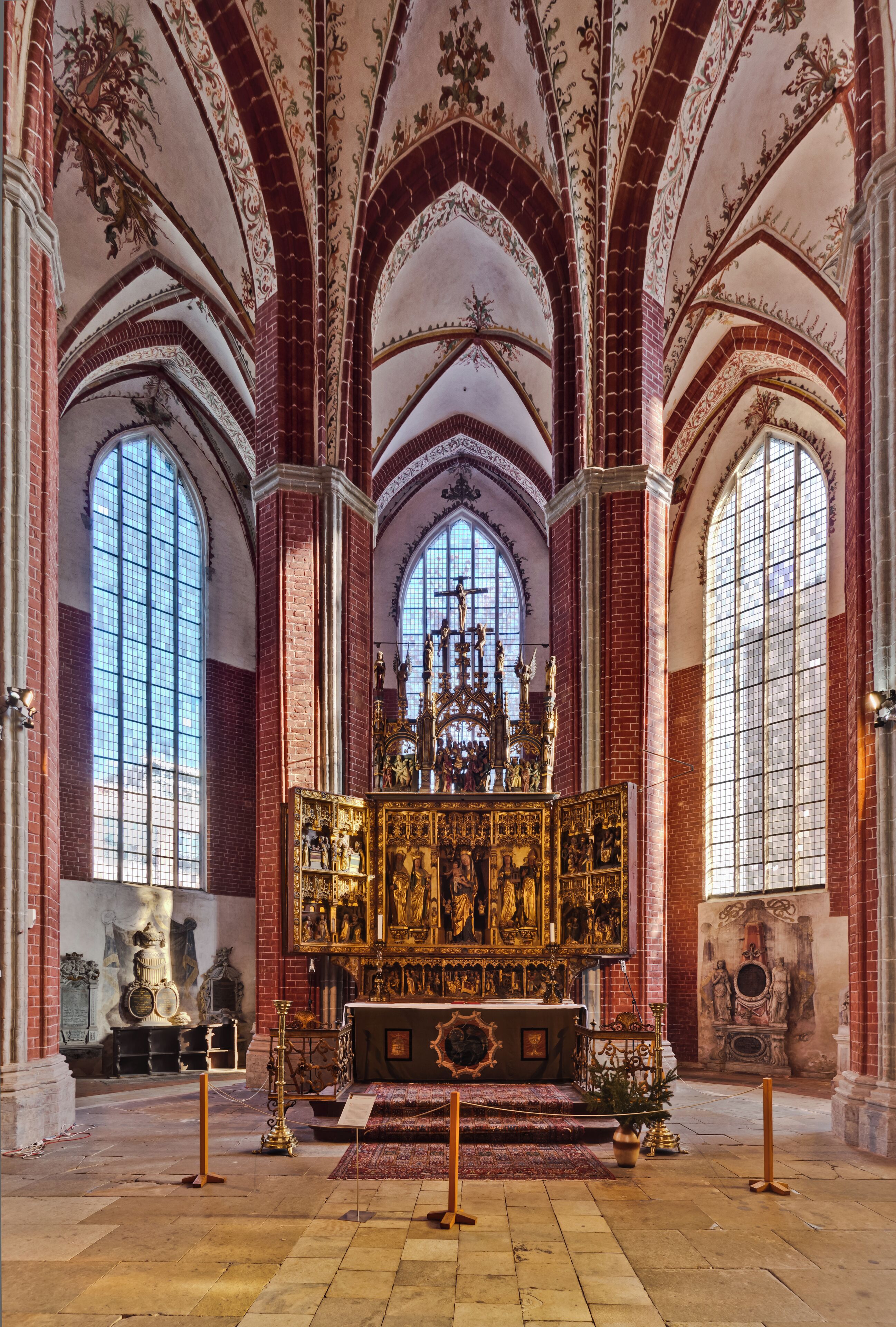 A church interior with red brick walls, large arched windows, and a central altar with religious statues.