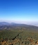 Een bergachtig landschap met dichte bossen en verre windturbines.