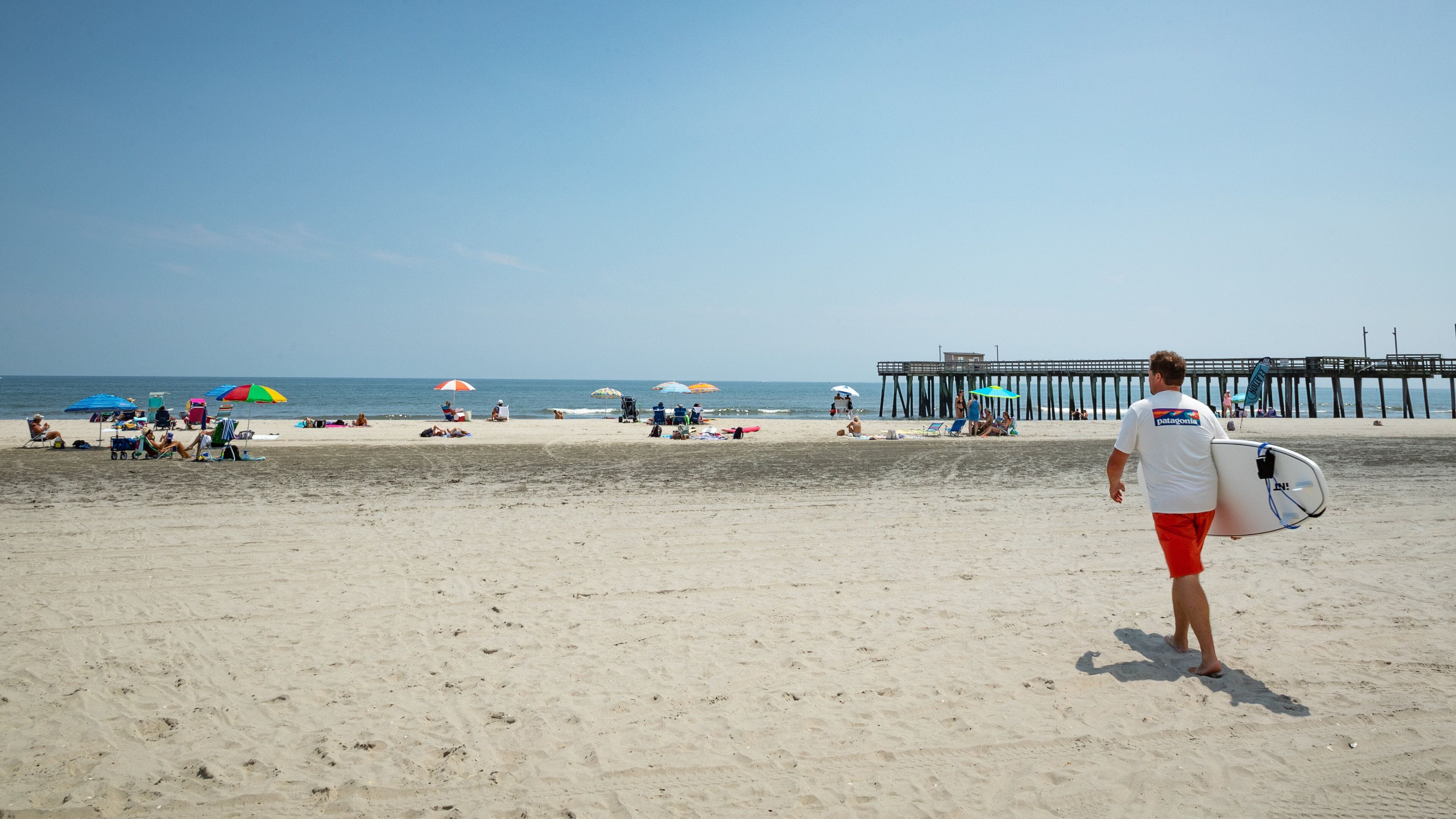 Una playa arenosa con sombrillas, un muelle y gente relajándose.