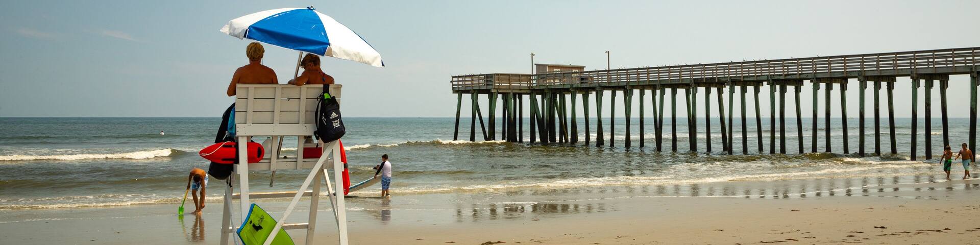 A beach with a lifeguard tower, a pier, and the ocean.