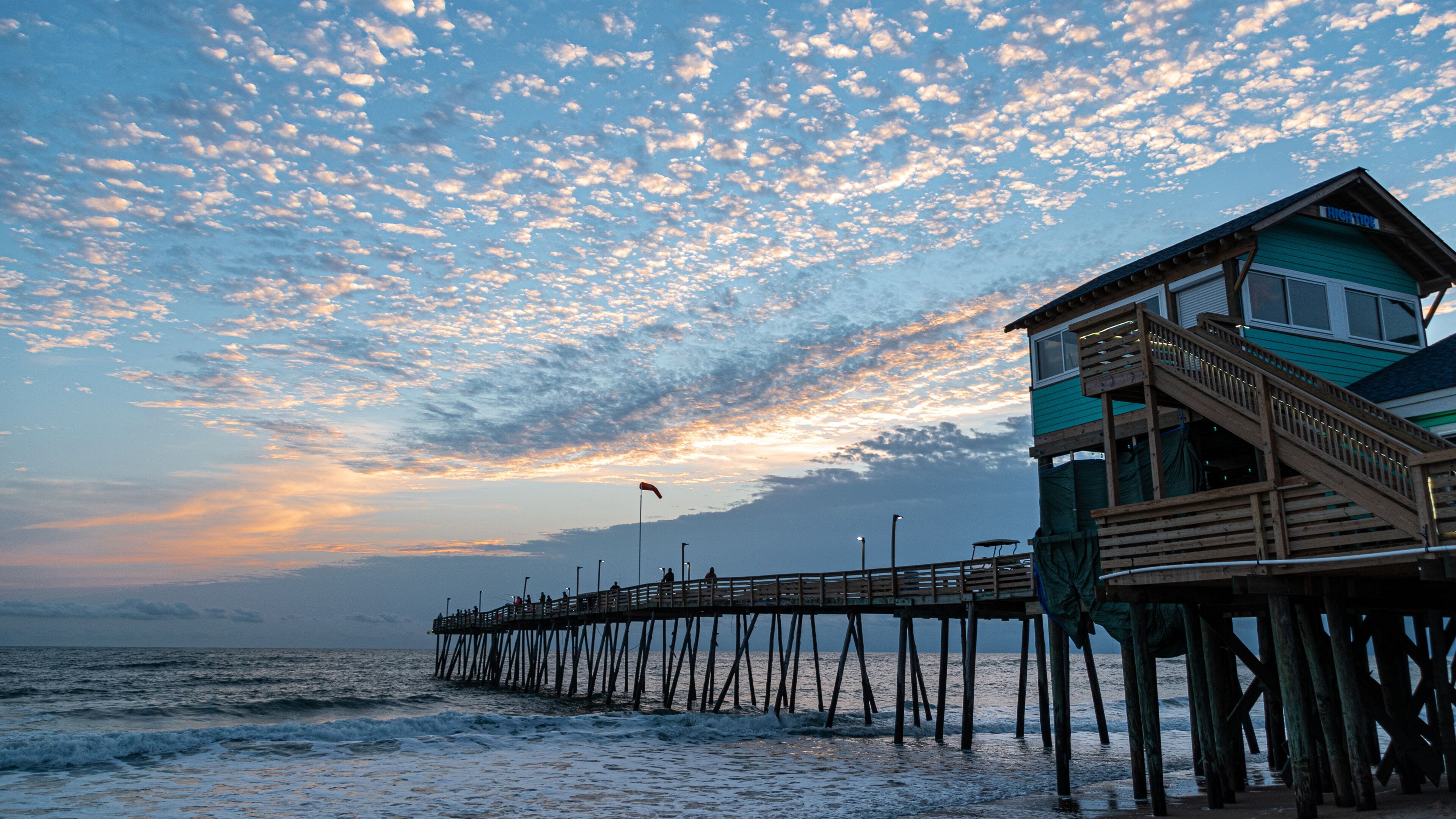 A wooden pier extending into the ocean with a lifeguard tower at the end.