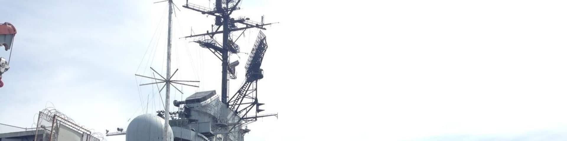 A military aircraft with a shark mouth design, number 205, parked near a naval ship.