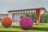 A large building with columns and a red emblem, surrounded by spherical flower arrangements.