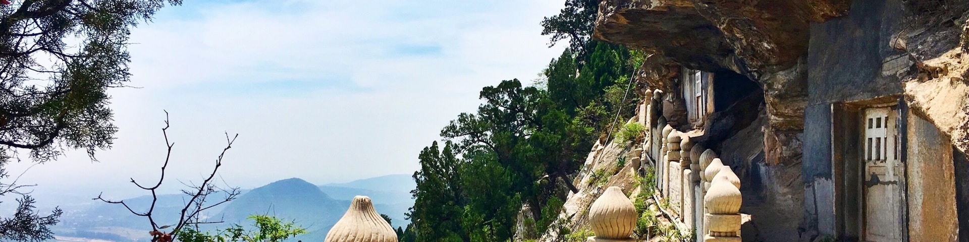 Un sentier de pierres menant à l’entrée d’une grotte, entouré d’une végétation luxuriante et dominé par un paysage montagneux.