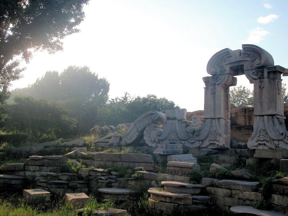 Ancient stone ruins with intricate carvings and columns, surrounded by greenery.