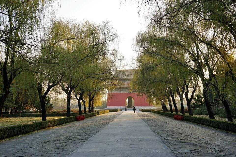 En asfalterad gångväg, omgiven av träd, leder fram till en röd byggnad med en valvformad ingång.
