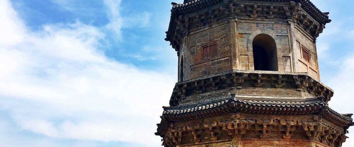 A large, ancient pagoda-style structure with a conical roof, surrounded by lush greenery and mountains in the background.