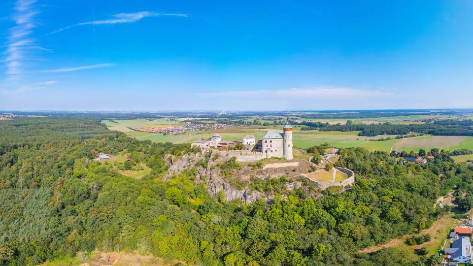 A castle on a hill surrounded by dense forest and a small village.