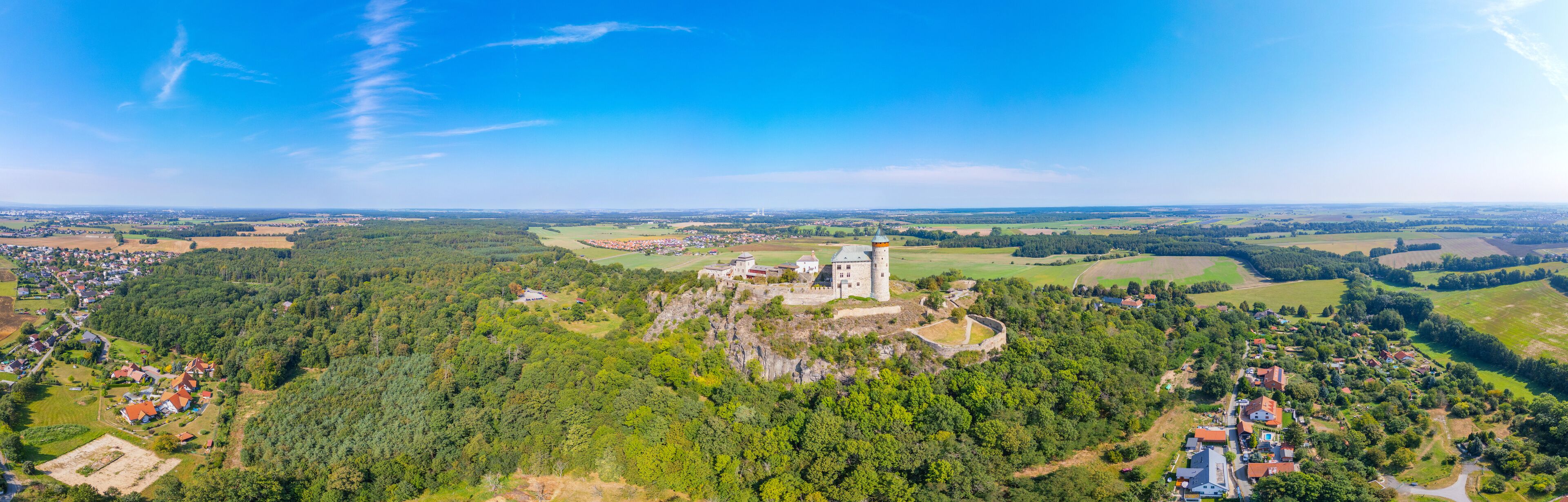A castle on a hill surrounded by dense forest and a small village.