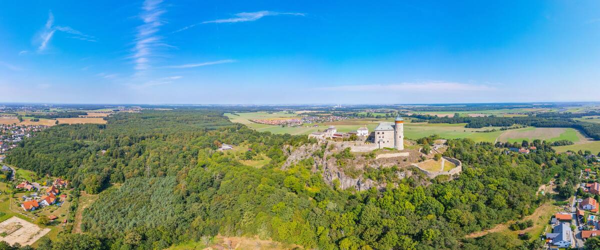 A castle on a hill surrounded by dense forest and a small village.