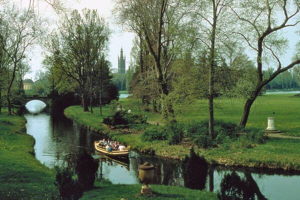 Un río con un puente, árboles y una barca con gente.