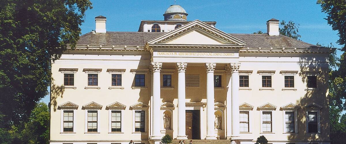 A large white building with columns and a dome, surrounded by a well-maintained lawn.