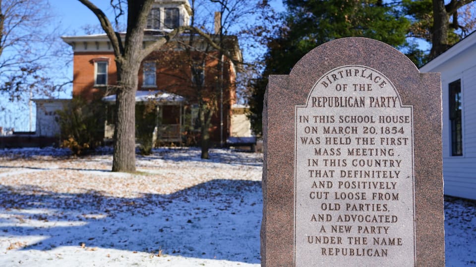 A historical marker in a snowy setting with a brick house in the background.