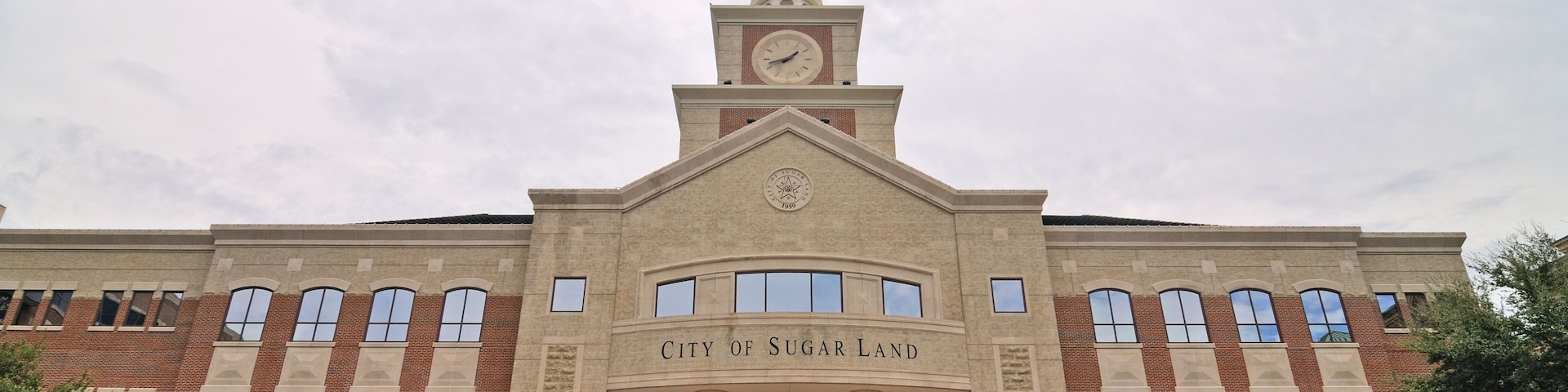 Um grande edifício de tijolos com uma torre do relógio e a inscrição 'City of Sugar Land'.